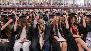 A group of graduates in caps and gowns flip the tassels on their caps.