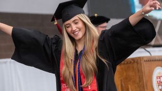 A young woman dressed in graduation regalia raises her hands in the air after receiving her diploma.