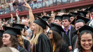 Graduates in caps and gowns celebrate during a commencement ceremony in a crowded arena.