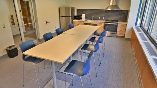 A kitchen setup in Whitman Hall featuring a fridge, stove, microwave and sink as well as a long table to seat 8 students