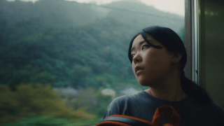 Film still from Chronicle of a City showing a woman looking out a train window.