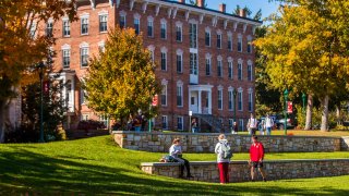 Saint Lawrence students walk about the quad on a sunny fall day. There are bright orange and red leaves scattered on the ground. 