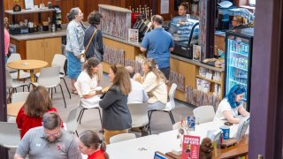 People gather at café tables and order food and drinks at a busy campus coffee shop.