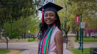 Francesca Mnenula wearing a graduation cap and cords on a college campus.
