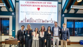 A group of seven individuals poses for a photo in front of a banner celebrating the renovation of the Hannon Room, acknowledging generous support from Jennifer Curley Reichert '90 and Paul Reichert.