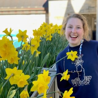 Grace Harkins with a wide smile stands among a garden of daffodils.