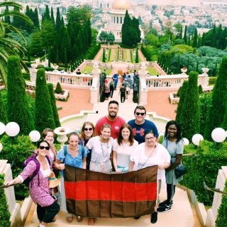 Group of students and faculty stand in a group on stairs with lots of greener in the back.