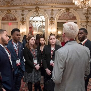 A group of students wearing business clothing stand spend with an alumnus during a networking event.