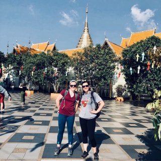 Two students stand on a tiled walkway in front of a large temple.