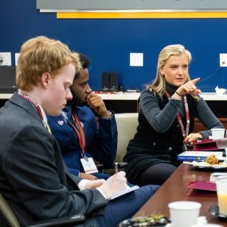 A panelist sits at the head of the table and engages with students who listen and take notes while she shares her career experiences.