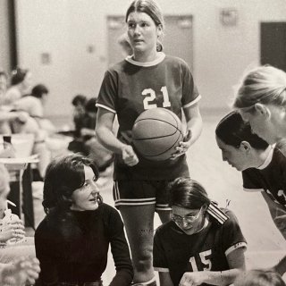 A black and white photo of Saints Women's Basketball huddled up on the sidelines of the court.