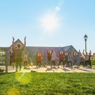 A yoga instructor guides a group of people through stretches on the Saint Lawrence University quad during a sunny day.