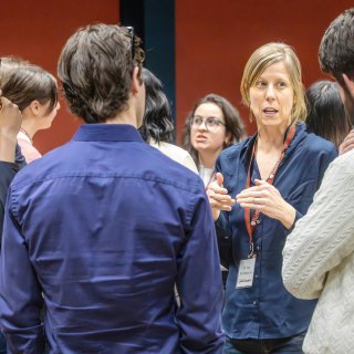 A group of people stands in a circle having a conversation, with one person speaking and gesturing while others listen attentively.