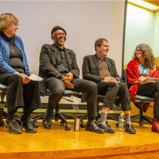 Four panelists sit on stage in chairs, smiling and engaged in conversation during an event at Saint Lawrence University.