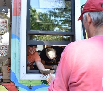 A person, wearing a Saint Lawrence hat, grabs food from a person working at a food truck.