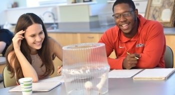 Two students, in a psychology class, view two live rats in a container on the desk.