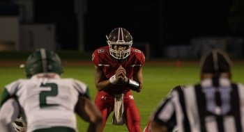 A Saint Lawrence football player, wearing a red jersey and helmet, prepares for the play on the football field.