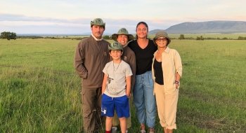 A family of five individuals gather for a photo on a grassy plain in Kenya.