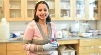 Professor Ana Estevez, wearing surgical globes, holds a test tube while standing in her lab.