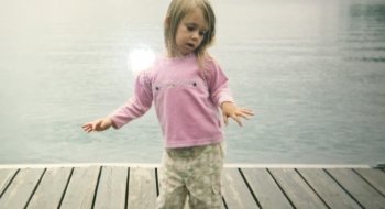 Brynn Afton as a small child around the age of three standing on a dock overlooking Saranac Lake.