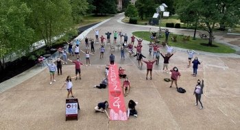 A large group of socially-distanced students stand outside holding a &quot;Class of 2024&quot; sign.