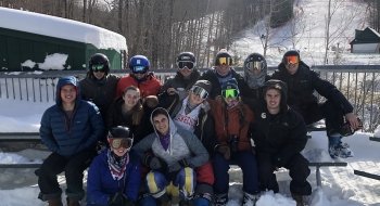 A group of Saint Lawrence club ski students sit on a snow covered bench at a ski mountain.