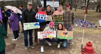 A group of seven student at a climate action vigil in a park square. They're holding handmade protest signs.