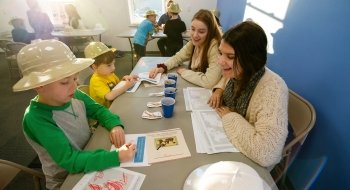 Two students work on a drawing project with two elementary school children.