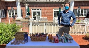 Conor McDermott, wearing a mask, stands behind a table with drinks and snacks on it.