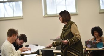 A professor hands a sheet of paper to a student in class.