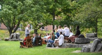A professor delivers a lecture to students seated on rocks and Adirondack chairs outside on the Saint Lawrence University campus.