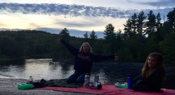 Two students sitting on a blanket on the rocks at the top of a waterfall at dusk.