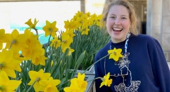 Grace Harkins with a wide smile stands among a garden of daffodils.