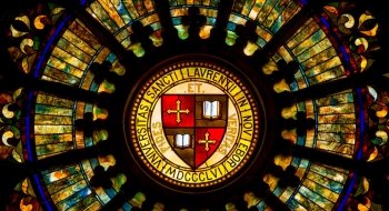 A decorative and elaborate stained-glass window with the Saint Lawrence University motto and shield at its center.