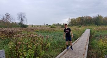 A student stands on a plank bridge over a gravel trail in a field of wildflowers.