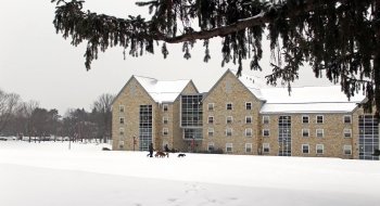 A modern stone residence hall on a gray day in winter. Snow covers the ground on the quad in front.