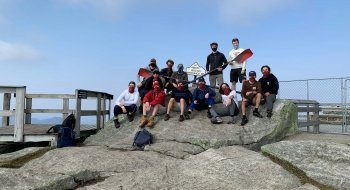 Twelve member of the Saint Lawrence Men's Rowing team at the peak of Whiteface Mountain, holding two rowing oars.