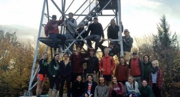 A large group of students gather for a photo at the base of a fire tower atop Mount Azure.