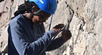 A student wearing a helmet and a harness, prepares to climb the rock face in front of them.