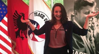 A Saint Lawrence student stands in front of the U.S. flag and the Peace Corps flag.
