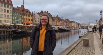 A student stands in front of a canal lined with old houses in Copenhagen.