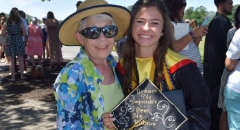 A recent graduate holds their decorated grad cap and smiles for a photo with her grandmother.