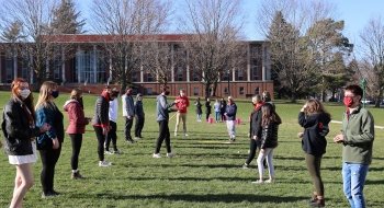 Students line up across from one another on a grassy quad on a sunny day.
