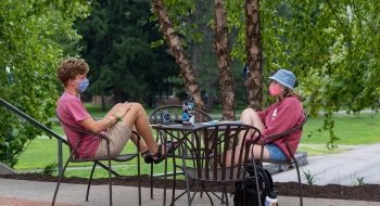 Two students sit at a small table on the walkway outside the Saint Lawrence Student Center on a bright fall day.