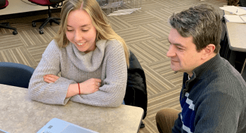 Sarah Campbell, sitting at a desk, looks at a laptop with professor Michael Shuckers.