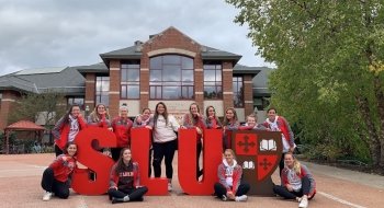 The Saint Lawrence volleyball team gathers around foam letters that spell out &quot;SLU&quot; in front of the Student Center.