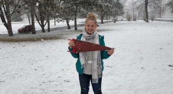 Abbie Cooper, holding a Saint Lawrence University pennant, stands in the snow in Canton, N.Y.