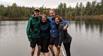 Four Saint Lawrence Adirondack Semester alumni, wearing rain jackets, stand on a dock over water in the Adirondack Park.