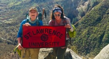 Saint Lawrence students, Elsa and Quinn, holding a red Saint Lawrence University flag, on the Har Ki Dun Trek.