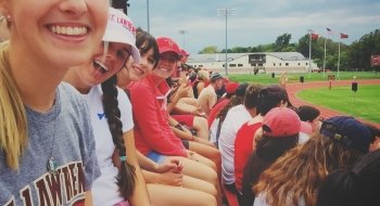 Saint Lawrence students, wearing Saint Lawrence t-shirts and hats, attend a football game.
